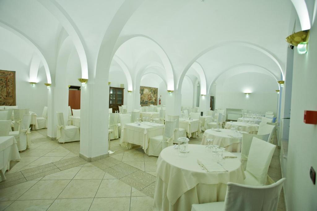 une salle à manger avec des tables blanches et des chaises blanches dans l'établissement Hotel Relais dei Normanni, à Monte SantʼAngelo