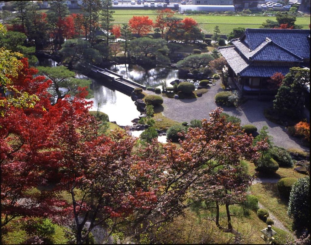 un jardin avec une rivière, un bâtiment et des arbres dans l'établissement Sansuien, à Yamaguchi
