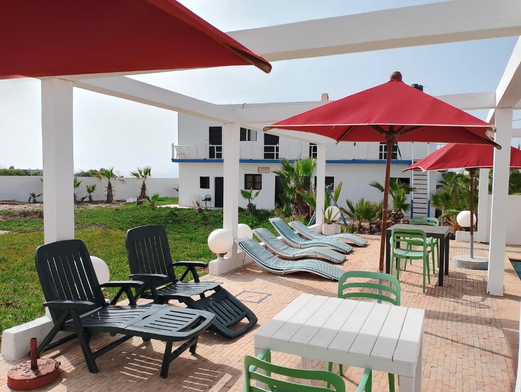 d'une terrasse avec des chaises, des tables et un parasol rouge. dans l'établissement Riad & Restaurant Ocean Beach Douira, à Agadir