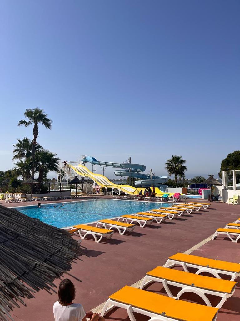 une piscine avec des chaises longues jaunes et un toboggan dans l'établissement Mobile Home 168 pour 6 pers Camping Siblu Lac des Rêves Perols, à Lattes