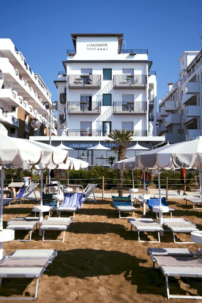 un groupe de chaises longues et de parasols devant un bâtiment dans l'établissement Hotel El Salvador Frontemare Piscina Riscaldata, à Lido di Jesolo