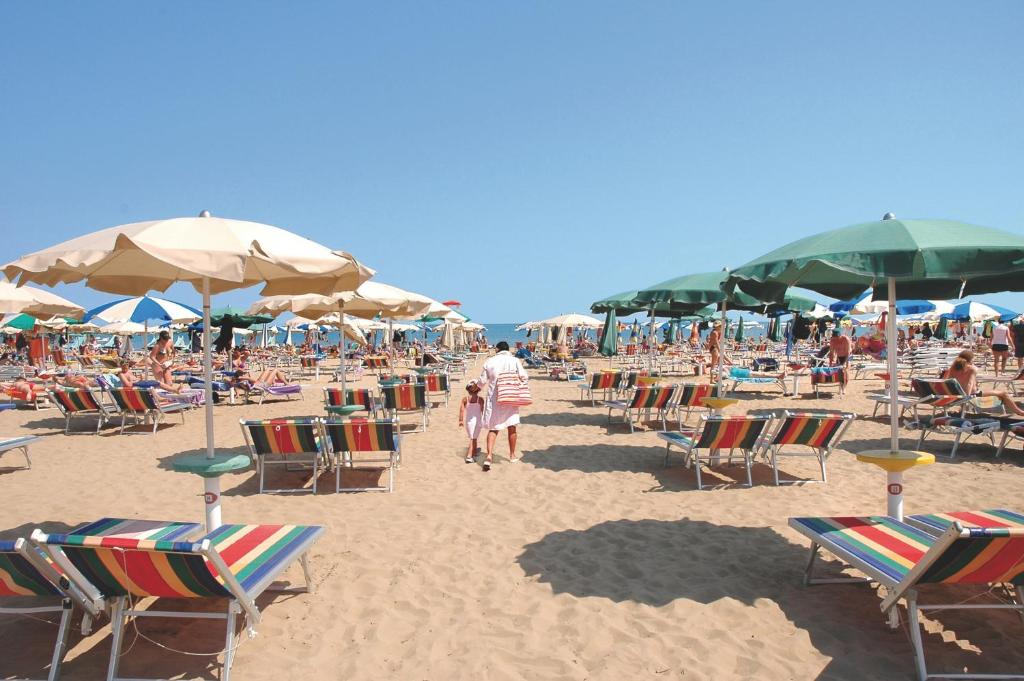 un groupe de chaises et de parasols sur une plage dans l'établissement Hotel Elvia, à Lignano Sabbiadoro