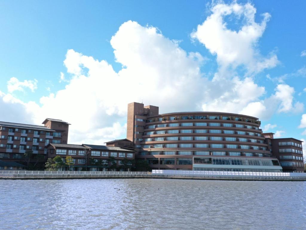 un grand bâtiment à côté d'un plan d'eau dans l'établissement APA Hotel & Resort Kaga Katayamazu Onsen Kasuikyo, à Kaga