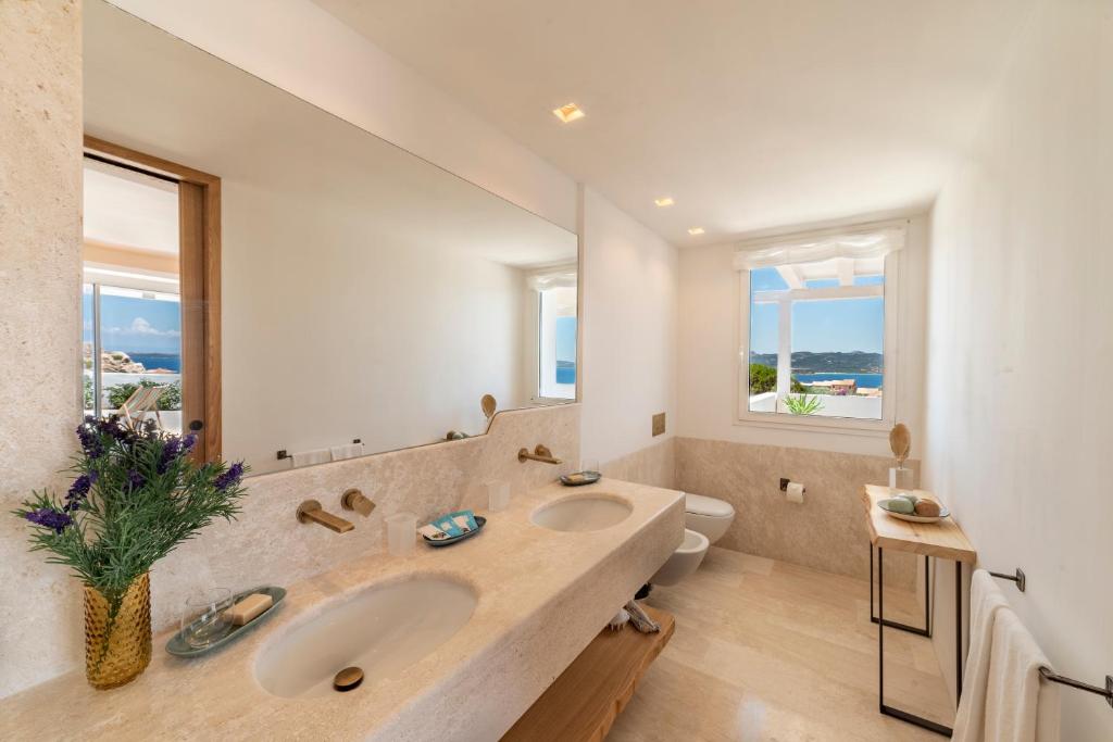 une salle de bain avec deux lavabos et un grand miroir dans l'établissement Hotel Grand Relais Dei Nuraghi, à Baja Sardinia