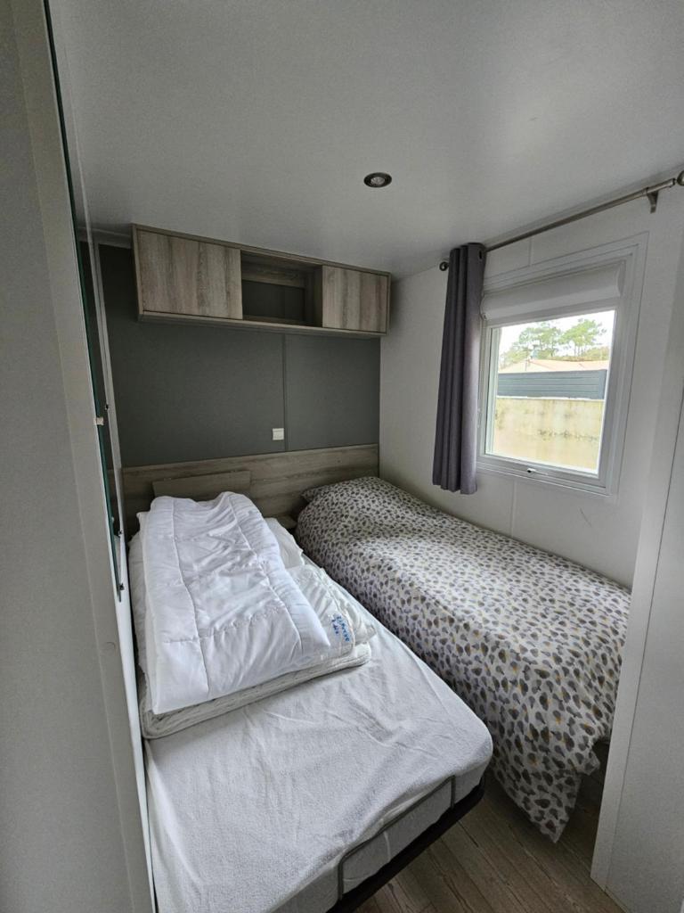 une petite chambre avec deux lits et une fenêtre dans l'établissement Grand Mobil Home A114, à Saint-Jean-de-Monts