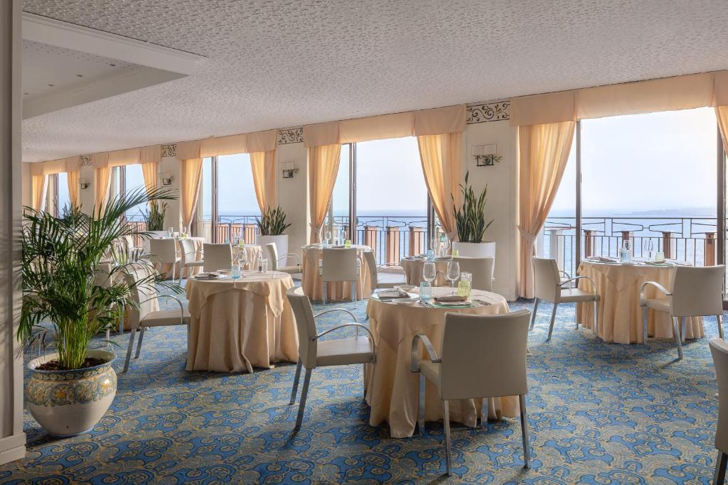 une salle à manger avec tables, chaises et fenêtres dans l'établissement UNA Hotels Capotaormina, à Taormine