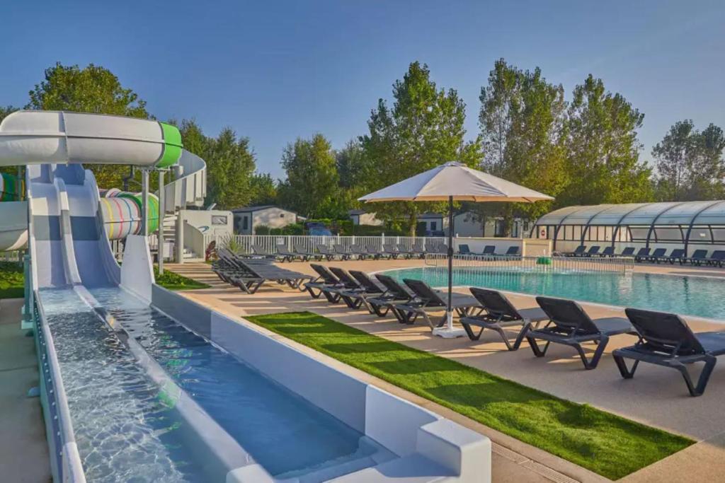 - une piscine dans un complexe avec des chaises et un parasol dans l'établissement Mobil Home 3 chambres, à Ouistreham