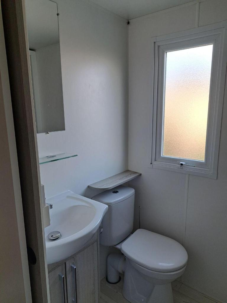une salle de bain avec toilettes, lavabo et fenêtre dans l'établissement mobil home 3 chambres 2 sdb 750, à Pont-Aven 5 autres photos