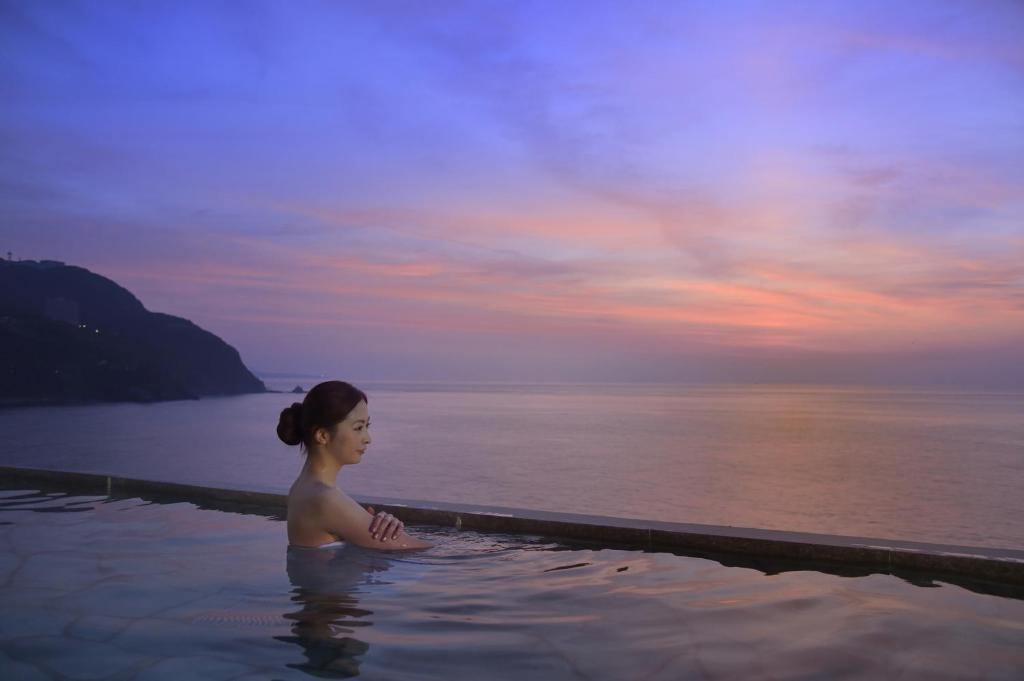 une femme assise dans une piscine à côté de l'eau dans l'établissement Hamanoyu, à Higashiizu