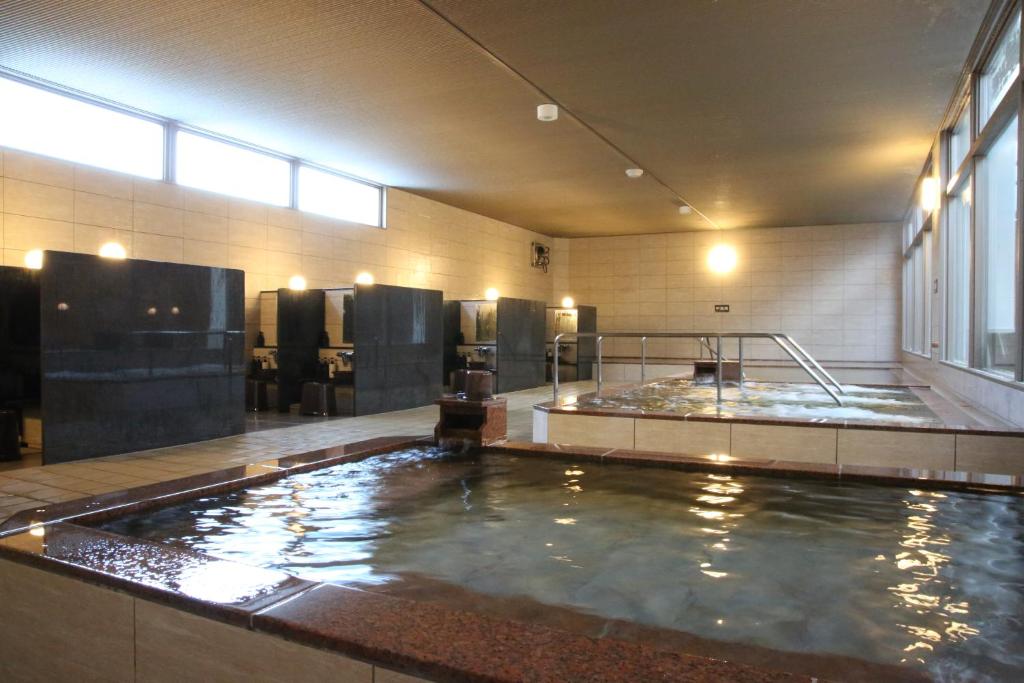 une salle de bains avec une grande piscine d'eau dans l'établissement Kojohama Onsen Hotel, à Shiraoi
