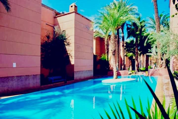 une piscine avec des palmiers à côté d'un immeuble dans l'établissement Riad DarDamia, à Marrakech