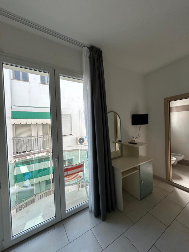 Cette chambre dispose d'une porte coulissante en verre, d'un bureau et d'une fenêtre. dans l'établissement Hotel Zamagna, à Cesenatico