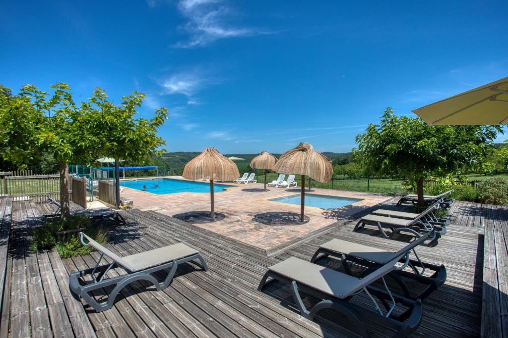 - une terrasse avec des chaises longues et des parasols à côté de la piscine dans l'établissement Domaine Les Pastourels, à Veyrines-de-Domme