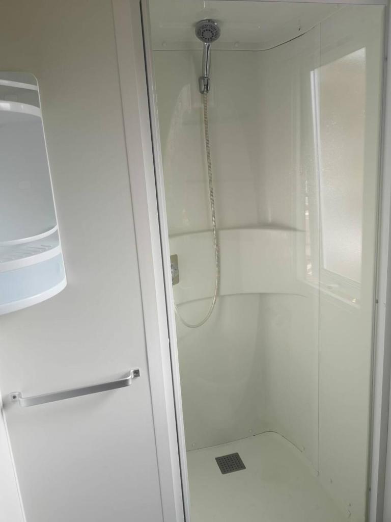 La salle de bains est pourvue d'une douche blanche avec une porte en verre. dans l'établissement CHEZ LOLO MH 3CH 2SDB CLIM 8p VUE CHAMPS EMPLACEMENT CALME, à Onzain