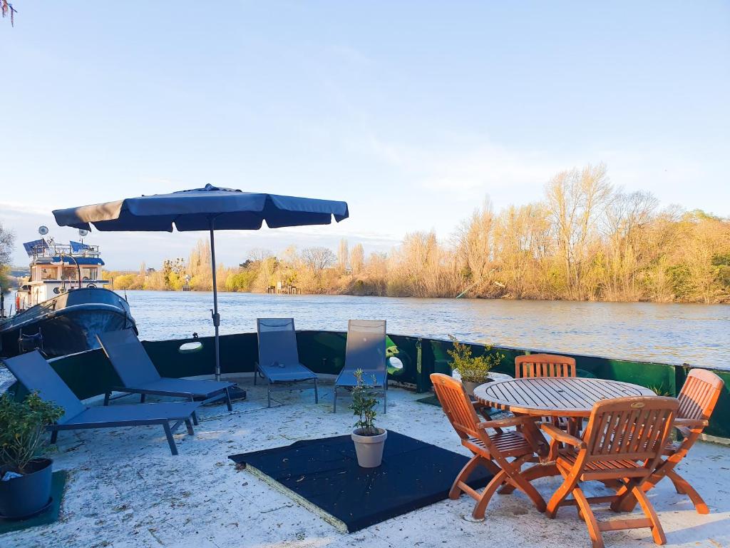 un patio avec des chaises, une table et un parasol dans l'établissement EXIGEHOME - Péniche 120 m2 en bord de Seine calme et verdoyant, à Le Port-Marly