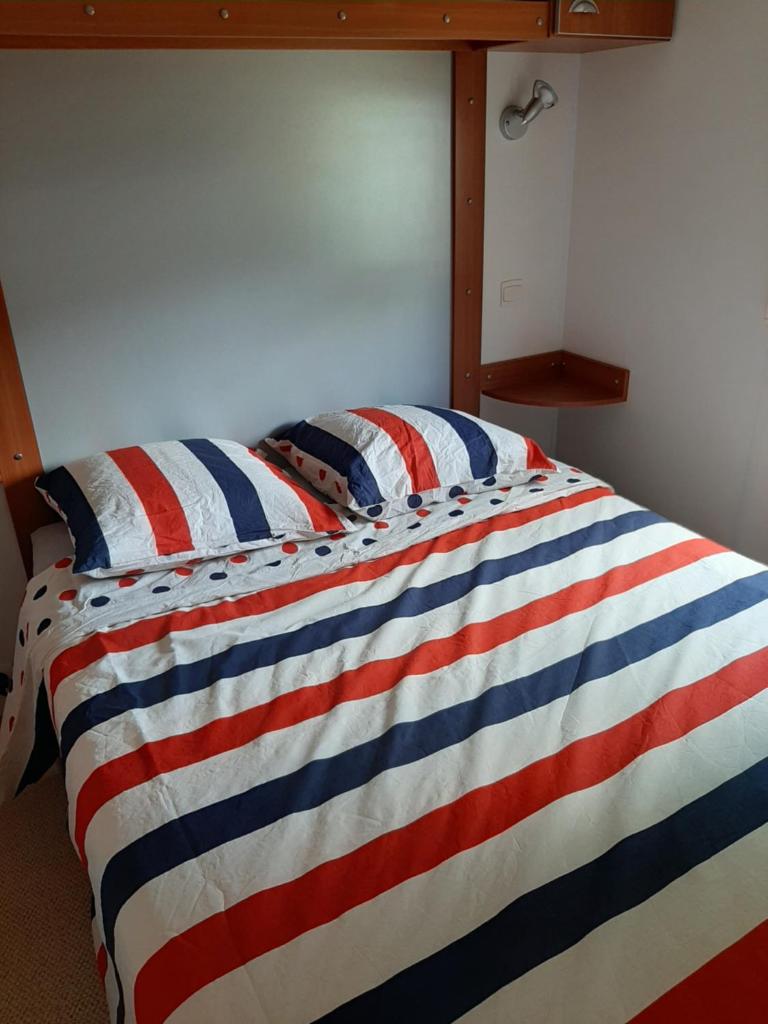 - un lit avec une couverture rouge rayée blanche et bleue dans l'établissement Mobil home, à Montrigaud