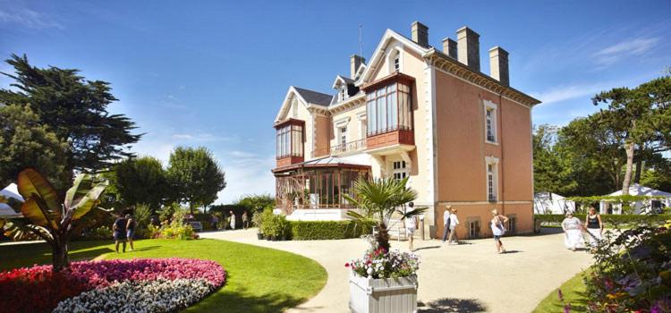 Une grande maison avec des gens qui marchent devant elle dans l'établissement Cottage Premium, camping 5* avec parc aquatique, à Hudimesnil