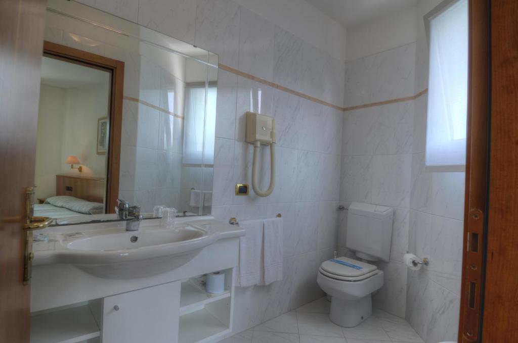 une salle de bain blanche avec un lavabo et des toilettes dans l'établissement Hotel Alisei, à Lignano Sabbiadoro