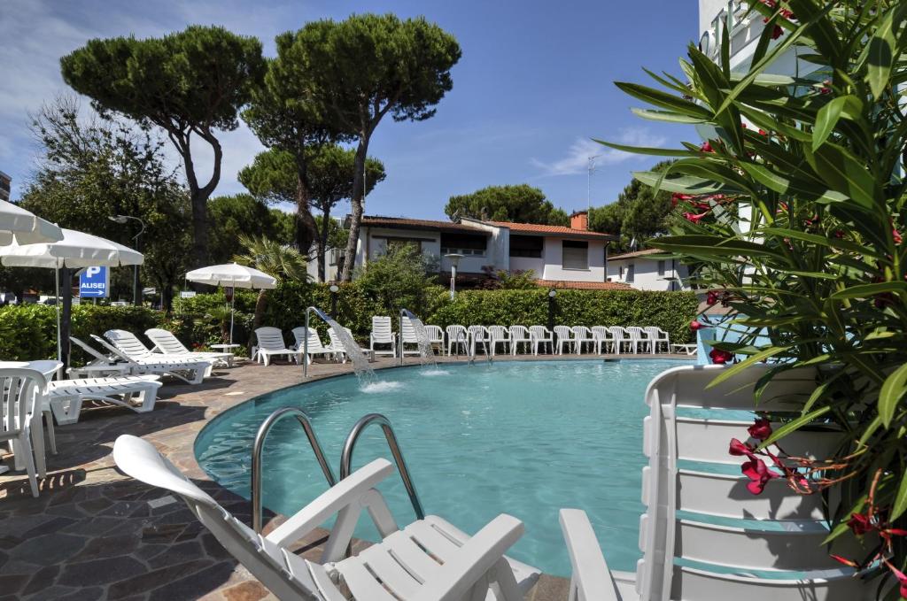 - une piscine avec des chaises blanches et un bouquet d'équipements dans l'établissement Hotel Alisei, à Lignano Sabbiadoro