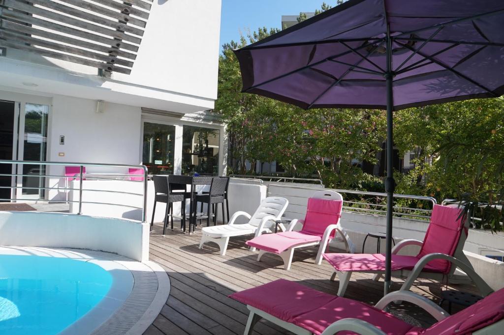 un patio avec des chaises et un parasol à côté d'une piscine dans l'établissement Hotel Anapaya, à Lignano Sabbiadoro