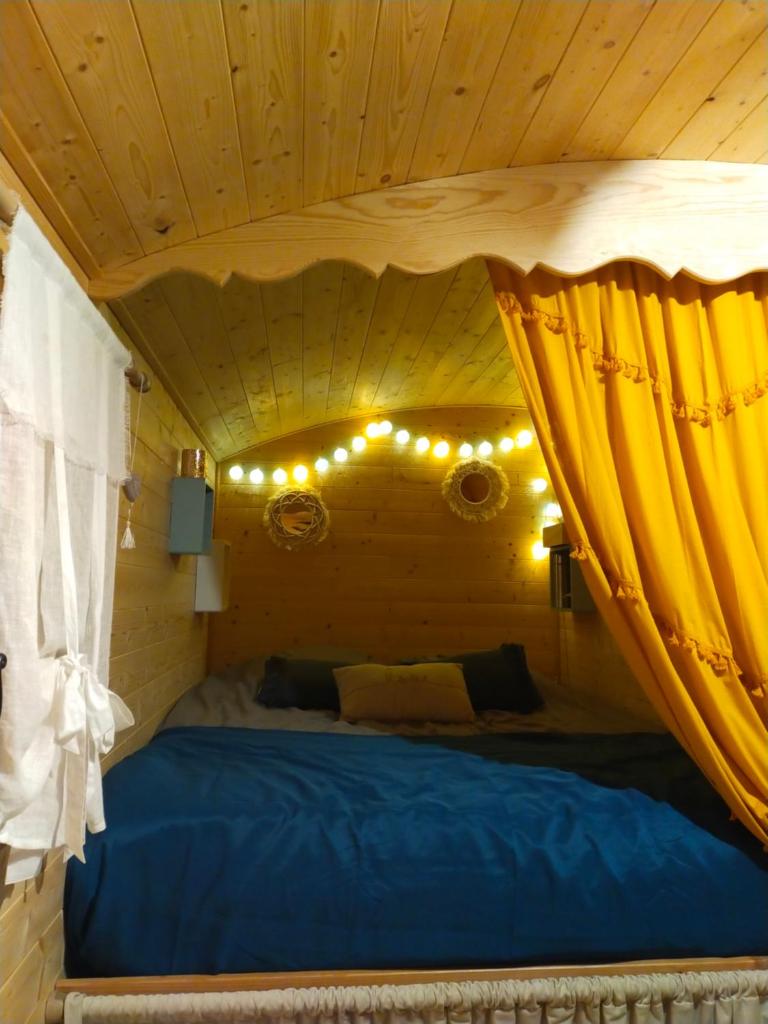 - une chambre dotée d'un lit avec des rideaux et des lumières jaunes dans l'établissement La roulotte D'elfes, à Thénac
