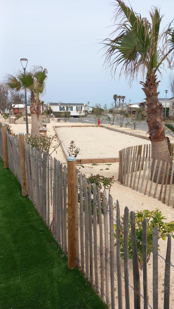 une clôture en bois à côté d'une plage bordée de palmiers dans l'établissement mobil home le castellas Bertrand /stehlin, à Sète