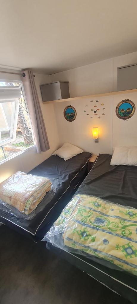 deux lits dans une petite pièce avec une fenêtre dans l'établissement MOBILHOME PREMIUM 3CH 6PERS, à Nans-les-Pins 37 autres photos