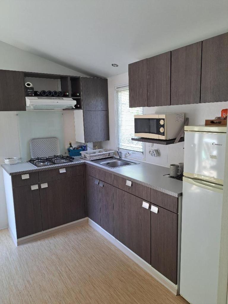 La cuisine est équipée de placards bruns et d'un réfrigérateur blanc. dans l'établissement Mobile Home 270, à La Roque-dʼAnthéron