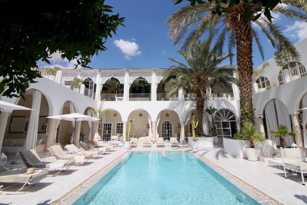 une piscine dans la cour d'un hôtel avec des chaises et des palmiers dans l'établissement Riad Palais Blanc & Spa, à Marrakech