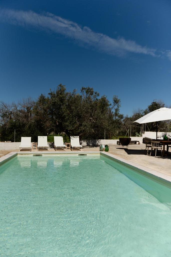- une piscine avec des chaises, une table et un parasol dans l'établissement Tenuta Lavati, Santa Maria di Leuca, à Castrignano del Capo