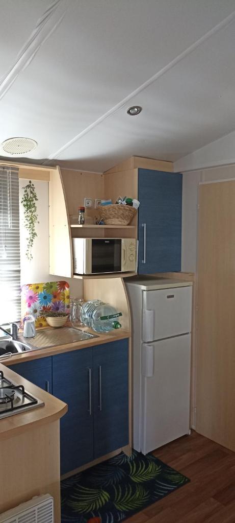 La cuisine est équipée de placards bleus et d'un réfrigérateur blanc. dans l'établissement Mobilhome L'Oasis Camping le Clos Cottet, à Angles