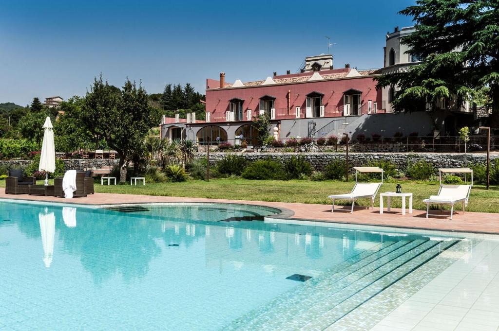 une piscine avec deux chaises et un bâtiment rose dans l'établissement Villa Eremo Sant'Emilia, à Trecastagni