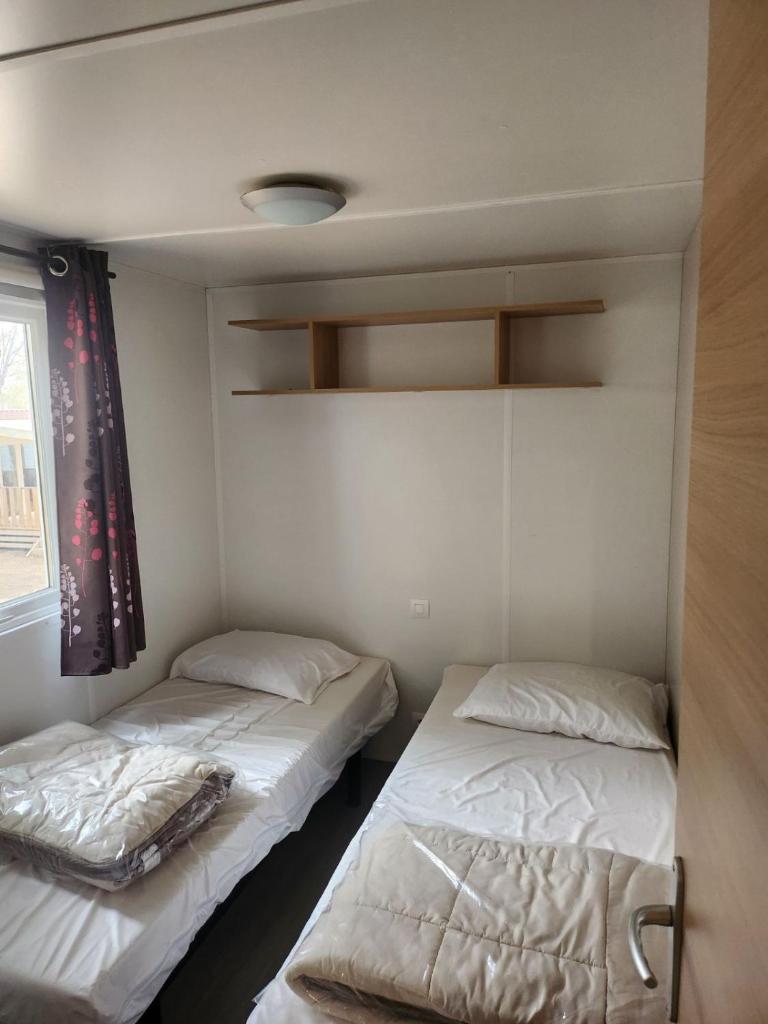 deux lits dans une petite pièce avec une fenêtre dans l'établissement MOBILHOME Lodge 3 chambres, 500m plage, camp 5 étoiles, à Vendres 37 autres photos