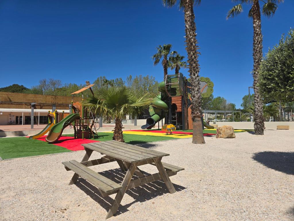 un parc avec un banc et une aire de jeux avec des palmiers dans l'établissement MOBILHOME Lodge 3 chambres, 500m plage, camp 5 étoiles, à Vendres