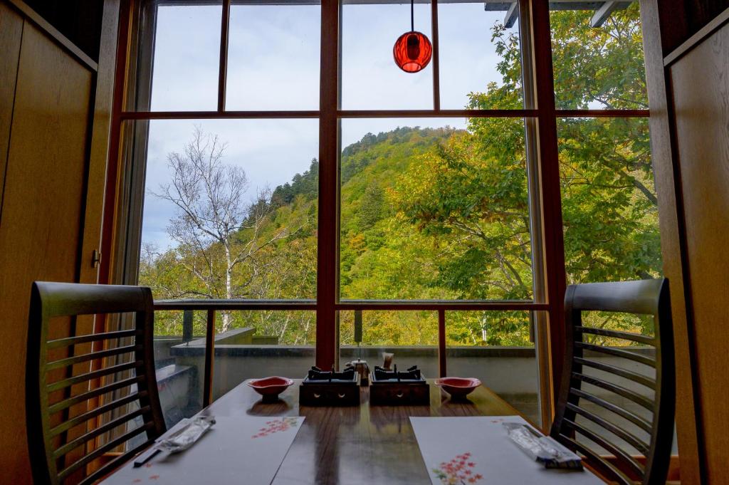 une salle à manger avec une grande fenêtre donnant sur une table dans l'établissement 志賀高原 白い温泉 渓谷の湯, à Yamanouchi
