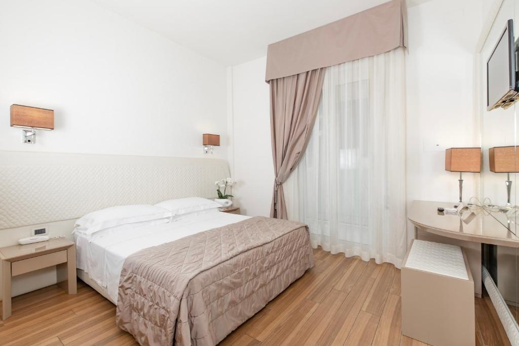 une chambre blanche avec un lit et un bureau dans l'établissement Hotel Alexander, à Milano Marittima