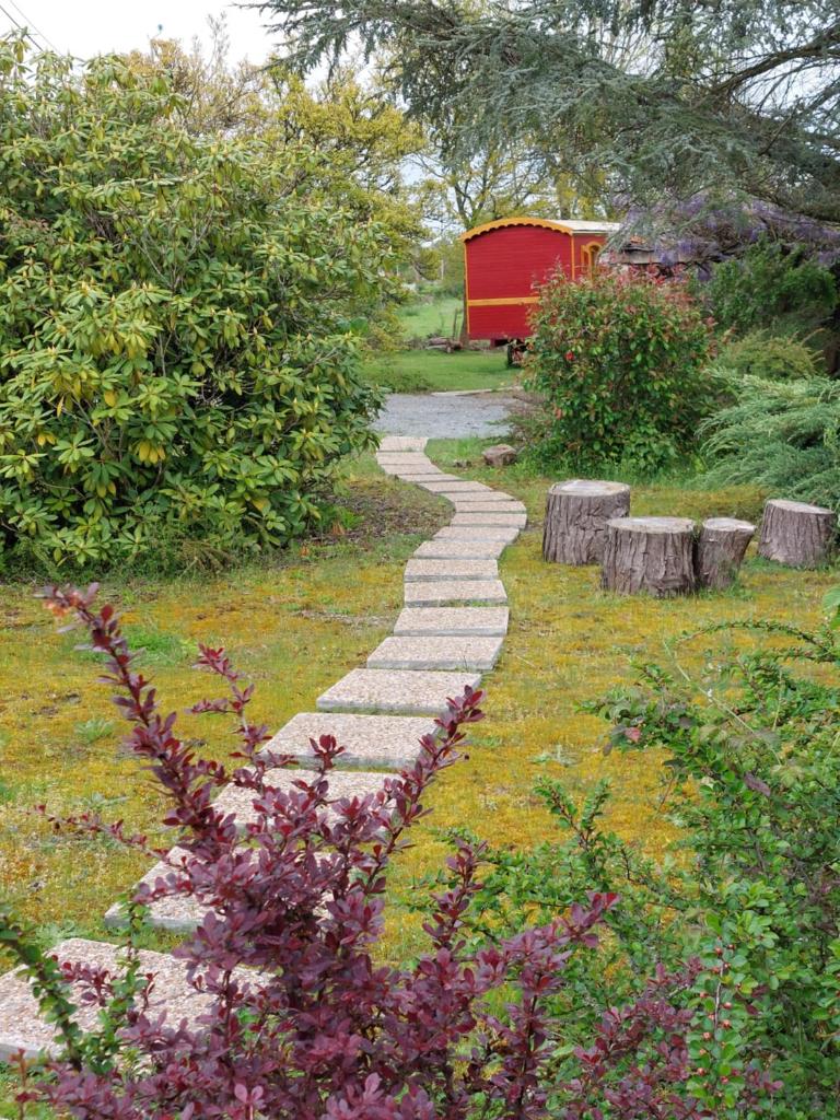 un chemin de pierre dans un jardin avec un hangar rouge dans l'établissement Roulotte ZEN, à La Saunière