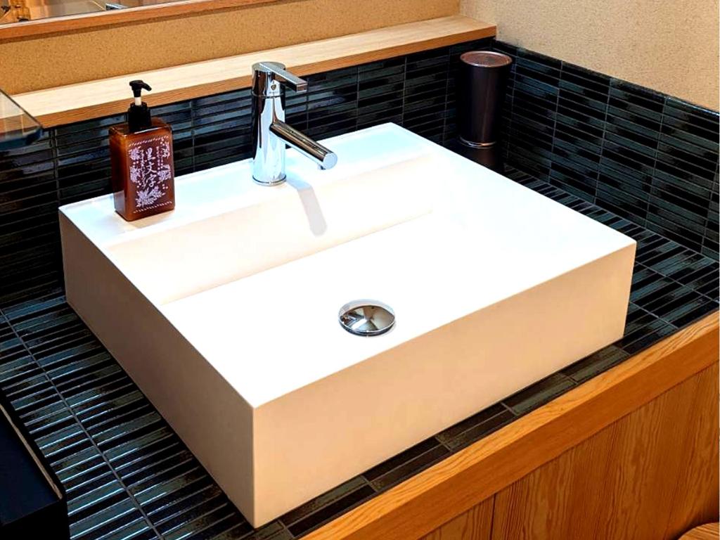 - un lavabo blanc dans la salle de bains revêtue de carrelage noir dans l'établissement Hanafubuki, à Itō