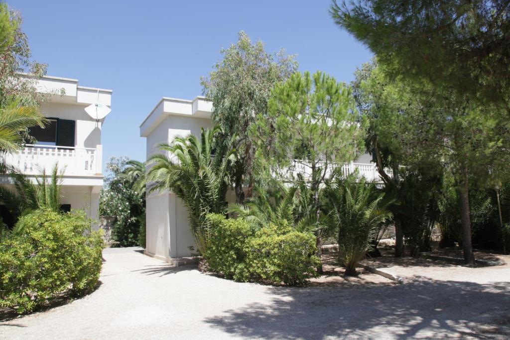 un bâtiment blanc avec des arbres et des buissons devant lui dans l'établissement Hotel dei Bizantini & Villaggio Campo dei Messapi, à San Pietro in Bevagna