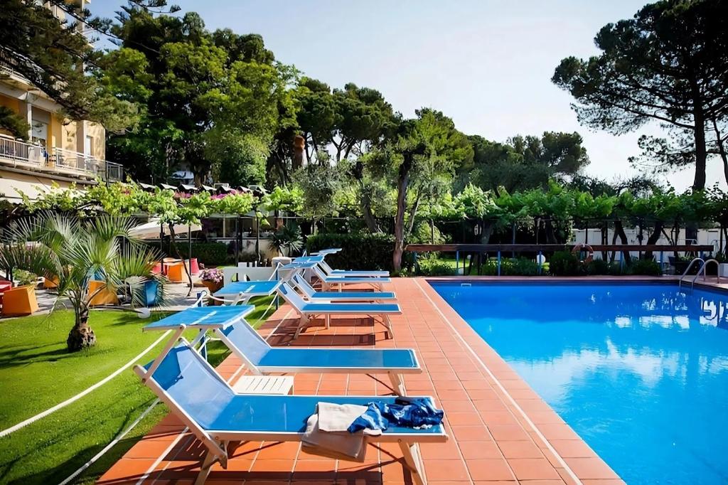 une piscine avec des chaises longues et un complexe hôtelier dans l'établissement Hotel Eden Park, à Diano Marina
