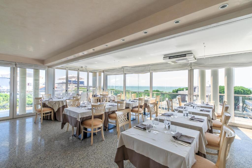 un restaurant avec des tables et des chaises blanches et des fenêtres dans l'établissement Hotel Villa Doimo, à Lignano Sabbiadoro