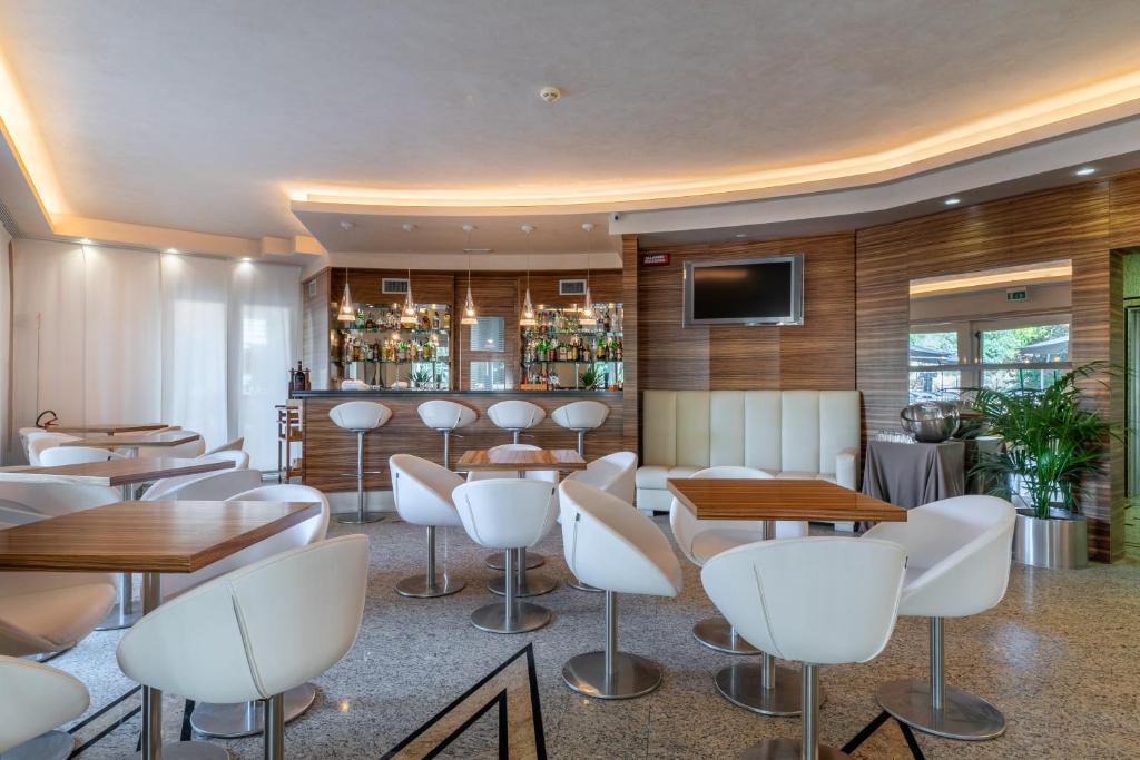 un restaurant avec des chaises et des tables blanches et un bar dans l'établissement Hotel Villa Doimo, à Lignano Sabbiadoro