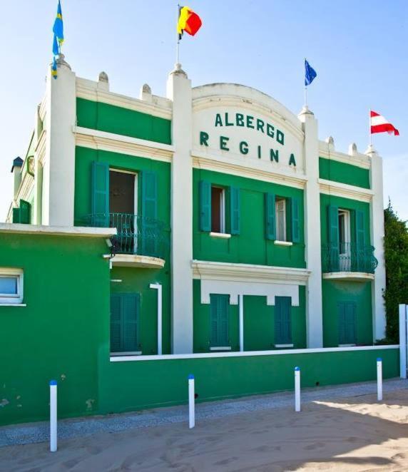 un bâtiment vert et blanc avec des drapeaux au sommet dans l'établissement Albergo Regina, à Senigallia