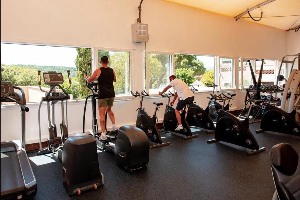 2 personnes faisant de l'exercice sur des vélos d'exercice dans une salle de sport dans l'établissement Mobil home climatisé golf de saint tropez camping 4 étoile, à Gassin