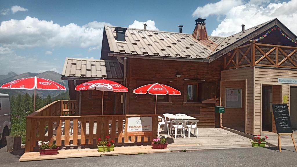 une maison en bois avec deux parasols rouges sur une terrasse dans l'établissement Yourte de montagne, à Colmars