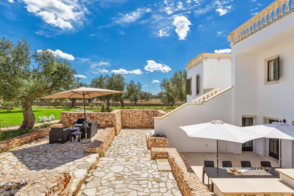 un patio avec des parasols, des tables et des chaises dans l'établissement Villa Cesira by Perle di Puglia, à Muro Leccese