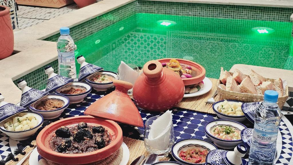 - une table avec des assiettes de nourriture et une piscine dans l'établissement Riad Diamant Bleu, à Fès