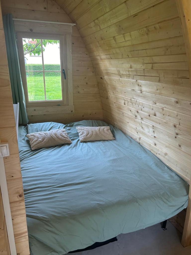 Ce lit se trouve dans une cabane en rondins dotée d'une fenêtre. dans l'établissement La pod de mon jardin, à Prix-lès-Mézières