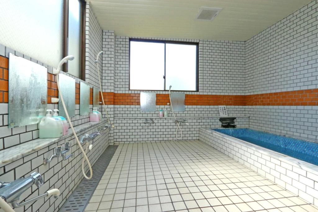 La salle de bains est pourvue de carrelage blanc, d'une baignoire et d'une fenêtre. dans l'établissement Sugakuso, à Yamanakako
