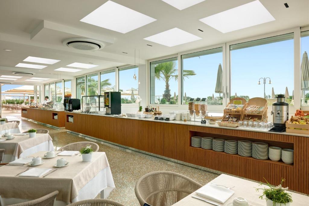 un restaurant avec des tables et des chaises et de grandes fenêtres dans l'établissement Hotel Aurora, à Lido di Jesolo